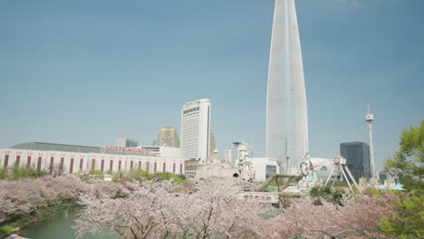 Seokchon-Lake-Park-With-Cherry-Blossoms,-Lotte-World-Tower,-And-Amusement-Park-In-Spring-In-Seoul,-South-Korea