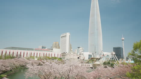 Parque-Del-Lago-Seokchon-Con-Flores-De-Cerezo,-Lotte-World-Tower-Y-Parque-De-Diversiones-En-Primavera-En-Seúl,-Corea-Del-Sur