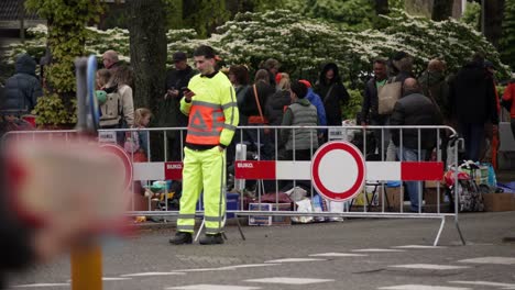 Traffic-controller-wearing-brightly-colored-clothes-stands-in-front-of-a-no-entry-sign-and-fence-during-King's-Day