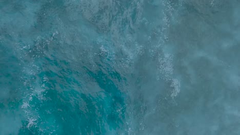 Top-Down-Slow-Motion-Drone-View-of-crystal-clear-water-and-crashing-waves-over-shallow-coral-reef-in-Uluwatu-Bali-Indonesia