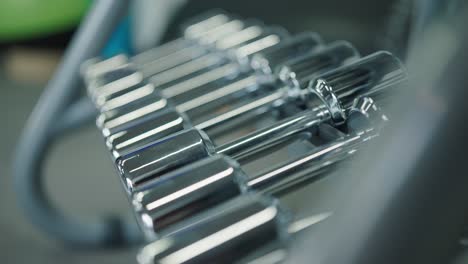 Sideways-reveal-of-shiny-metallic-dumbbell-rack-at-indoor-gym-facility