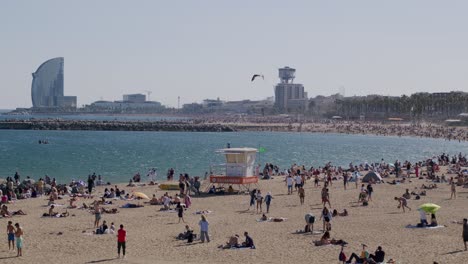 Crowded-Barcelona-beach-on-sunny-day,-city-skyline-in-background,-blue-sky