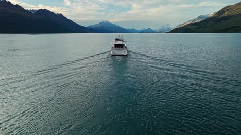 Yacht-pulls-away-from-aerial-overview-entering-Lake-Wakatipu-to-snowy-mountains