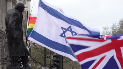 A-blue-and-white-Star-of-David-Israeli-flag-flies-with-a-Union-Jack-British-flag-and-a-rainbow-Pride-flag-next-to-the-statue-of-Winston-Churchill-on-Parliament-Square