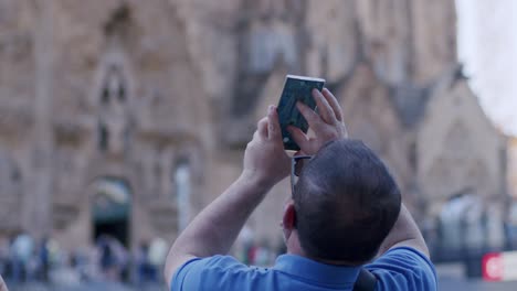 Mann-Im-Blauen-Hemd-Nimmt-Die-Sagrada-Familia-Mit-Smartphone-Auf,-Touristen-Im-Hintergrund,-Tagsüber,-Barcelona
