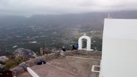 Hikers-Sit-on-Mountain-Top-and-Enjoy-Epic-360-Degree-Viewpoint-High-Above-Cliff