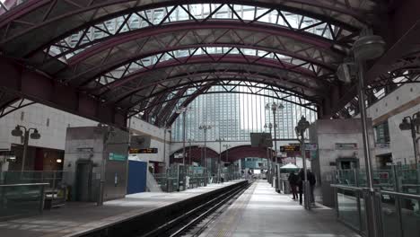 Observando-El-Andén-De-La-Estación-DLR-Canary-Wharf-En-Londres-Con-Viajeros,-Ilustrando-El-Concepto-De-Conectividad-Y-Movilidad-Urbana-Moderna.