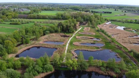 Aerial-view-of-belgian-countryside-with-pathway-going-through-nature-reserve,-ponds,-forest-and-agricultural-landscape