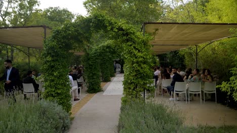 Toma-En-Cámara-Lenta-De-Invitados-Sentados-Junto-A-Los-Arcos-De-Césped-En-La-Recepción-De-La-Boda