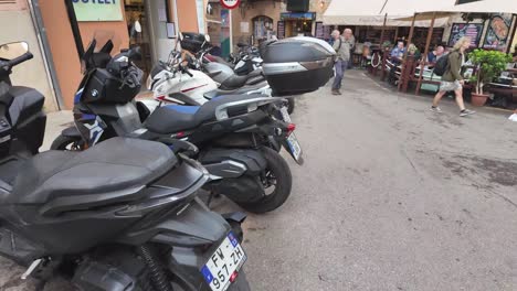 Palma-De-Mallorca-street-style-with-motorcycles-and-scooters-parked,-people-walking-and-shopping,-small-terrace-and-coffee-shop