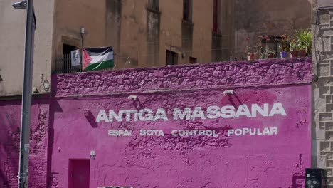 Man-in-silhouette-walking-past-a-vibrant-pink-wall-with-political-graffiti-in-Barcelona,-daylight