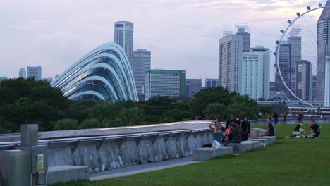 Marina-barrage-rooftop-urban-park,-static-shot-capturing-people-picnic-and-hangout-on-the-green-grass-with-Singapore-Flyer-observation-wheel-and-gardens-by-the-bay-in-the-background