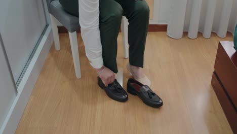 Close-up-of-person-sitting-and-tying-elegant-black-dress-shoes-indoors