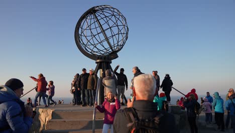 Turistas-Tomando-Fotos-Bajo-El-Monumento-Del-Globo-En-El-Cabo-Norte-De-Noruega-Al-Atardecer-A-60-Fps