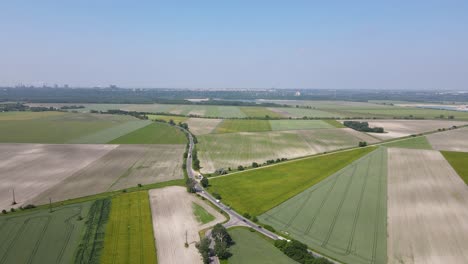 Vista-Aérea-De-Los-Automóviles-Que-Circulan-Por-La-Carretera-A-Lo-Largo-De-Los-Campos-Verdes-En-Szalkszentmarton,-Hungría