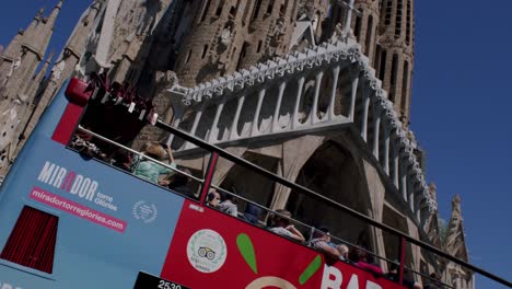 Tourists-on-sightseeing-bus-admiring-the-Sagrada-Familia-in-Barcelona-under-clear-blue-sky,-midday-light