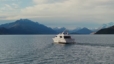 Aerial-sideview-tracking-follows-yacht-with-epic-snow-capped-mountains-behind