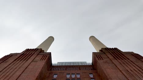 Blick-Auf-Die-Ikonischen-Türme-Des-Kraftwerks-Battersea-In-London,-über-Denen-Ein-Flugzeug-Vorbeifliegt