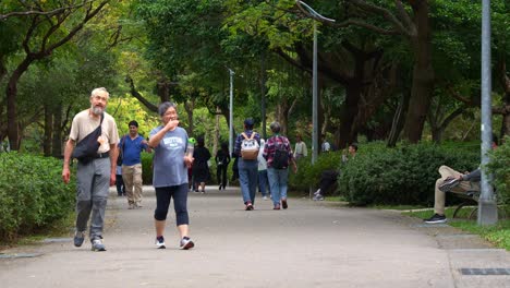 Elderly-and-family-walking-through-strolling-path-of-Daan-forest-park,-an-ecological-lush-forest-environment-in-the-bustling-city-center-of-Taipei,-Taiwan