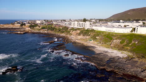 Drohnenansicht-Bei-Sonnenaufgang-über-Der-Küste-Von-Hermanus,-Während-Die-Bewohner-In-Einem-Gezeitentümpel-Schwimmen