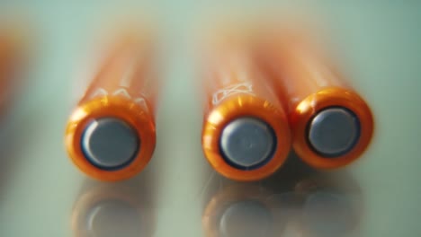 Macro-video-of-a-pile-of-rolling-batteries-on-a-desk-with-reflection,-golden-battery,-slow-motion-120-fps