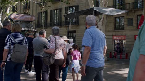 Pedestrians-strolling-near-a-street-performer-on-Barcelona's-vibrant-La-Rambla,-sunny-day