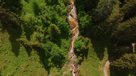 Antena-De-Un-Pequeño-Arroyo-De-Montaña-Rodeado-Por-Un-Bosque-Verde-Y-Una-Pradera