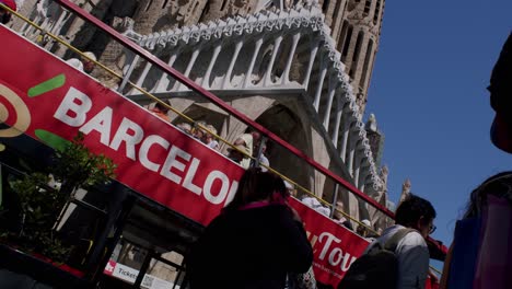 Low-angle-shot-of-Sagrada-Familia-with-clear-blue-sky,-tourists-visible,-Barcelona-tour-bus-in-foreground