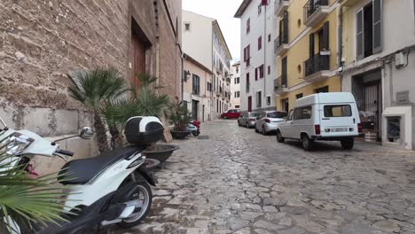 Eine-Gasse-In-Palma-De-Mallorca-Mit-Typischer-Mallorquinischer-Architektur,-Autos,-Oldtimern-Und-Motorrädern,-Die-Auf-Der-Straße-Geparkt-Sind