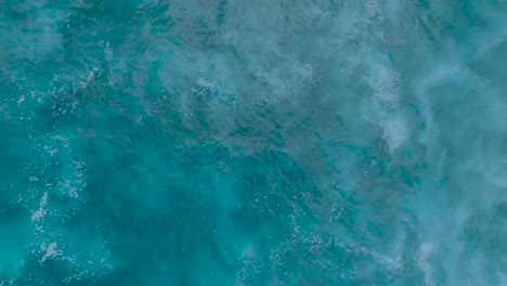Top-Down-Slow-Motion-Drone-View-of-turquoise-clear-water-and-crashing-waves-over-shallow-coral-reef-in-Uluwatu-Bali-Indonesia