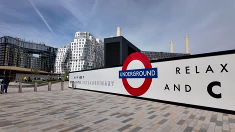 Fuera-De-La-Central-Eléctrica-De-Battersea-Con-El-Icónico-Cartel-Subterráneo-TFL-Roundel-Con-Modernos-Apartamentos-En-Segundo-Plano