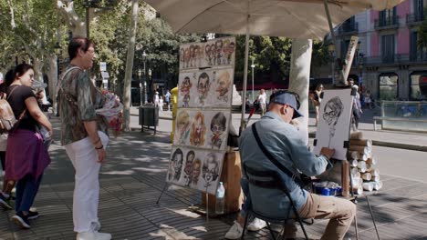 Street-artist-drawing-portraits-for-tourists-in-a-busy-Barcelona-square,-sunny-day