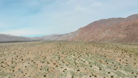 Aerial-shot-lifting-up-showcasing-the-dry-desert-landscape-surrounded-by-Mountains-on-a-bright-sunny-day