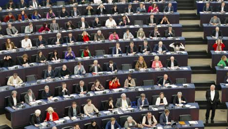 European-politicians-of-parliament-putting-on-headset-and-voting-in-the-EU-parliament-hall-in-Strasbourg,-France---Panning-shot
