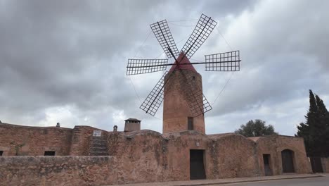 Straße-Mit-Kreuzung,-Traditioneller-Windmühle-Und-Architektur-Mit-Dramatischem-Himmel-Im-Hintergrund