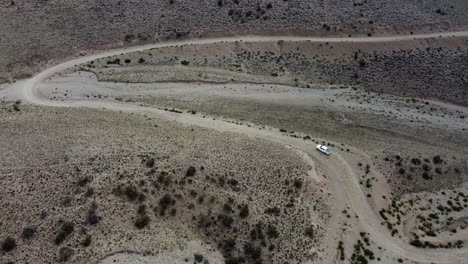 Aerial-follows-truck-driving-winding-dirt-road-in-arid-hill-landscape