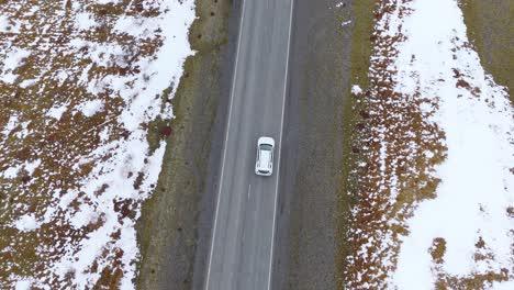 Aerial-Drone-Top-Down-White-Car-Drive-through-snowy-dry-grass-side-of-road-track