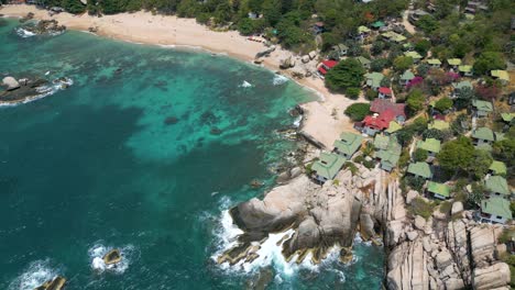 Slow-rotating-aerial-drone-shot-over-houses-perched-on-cliffs-on-tropical-island