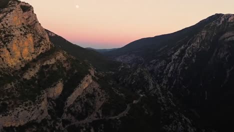 As-the-sun-sets,-casting-a-golden-glow-over-the-mountain-range,-a-small-moon-emerges-on-the-horizon,-evoking-the-enchanting-allure-of-nature-and-igniting-a