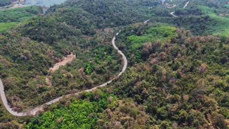 Bird's-eye-view-of-a-road-winding-through-the-forest-in-Songklaburi,-Thailand,-surrounded-by-lush-greenery