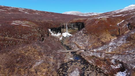 Skyline-Mountain-Background-in-Svartifoss-Icelandic-Waterfalls-Aerial-Drone-Zoom-into-cascading-water,-black-hidden-national-park-landscape