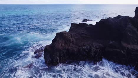 drone-footage-circling-around-a-rocky-volcanic-peninsula-as-the-white-capped-waves-of-the-blue-ocean-water-crash-onto-the-rocky-ledge-on-the-island-of-Oahu-in-the-Hawaiian-islands