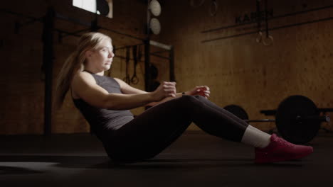 Real-time-of-blonde-fitness-junkie-doing-sit-ups-in-gym,-cinematic-lighting