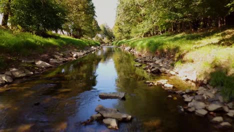 Fluss-Mit-Steinen-Und-Bäumen-Am-Rande,-Filmischer-Drohnenschuss