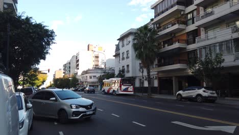 Urban-avenue,-cars-drive-by-skyline-palm-tree-city-of-buenos-aires-argentina-sky-vehicles-traffic,-Carabobo-and-directorio-avenue