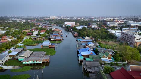 Un-Disparo-De-Un-Dron-Siguiendo-A-Un-Bote-De-Cola-Larga-Deslizándose-Sobre-Un-Canal-En-Un-Suburbio-En-Las-Afueras-De-Pak-Kret,-Tailandia