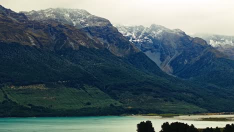 Una-Capa-Brumosa-De-Nubes-A-Través-De-Montañas-Cubiertas-De-Nieve-Domina-Aguas-Tranquilas-En-Nueva-Zelanda