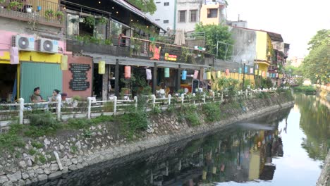 Serene-city-scenery,-still-water,-people-relax,-cafe-business-building