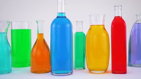 Close-up-footage-of-transparent-glass-bottles-with-colored-water,-white-background