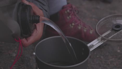 Two-women-on-a-backpacking-trip-pour-water-into-a-camp-stove-to-cook-a-dehydrated-meal-in-the-Olympic-Peninsula---Washington-State